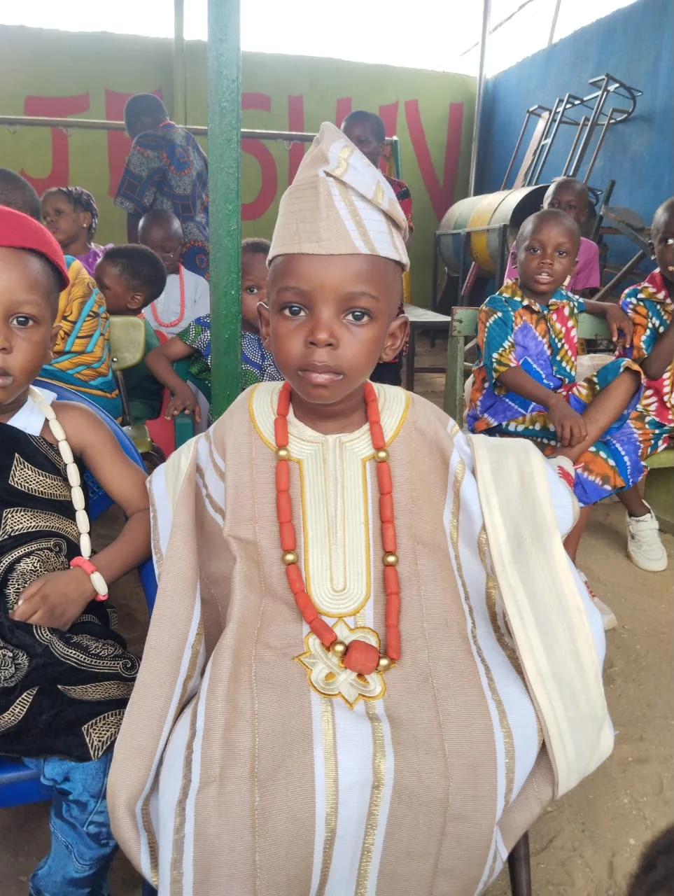 A young pupil in a cream agbada and fila with coral beads